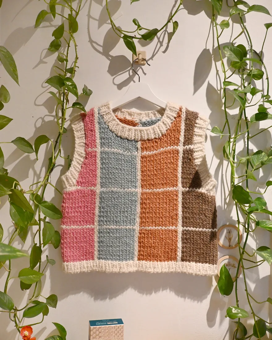 A hand-knitted colour-block vest on a hanger among trailing plants in the Knytfolket shop